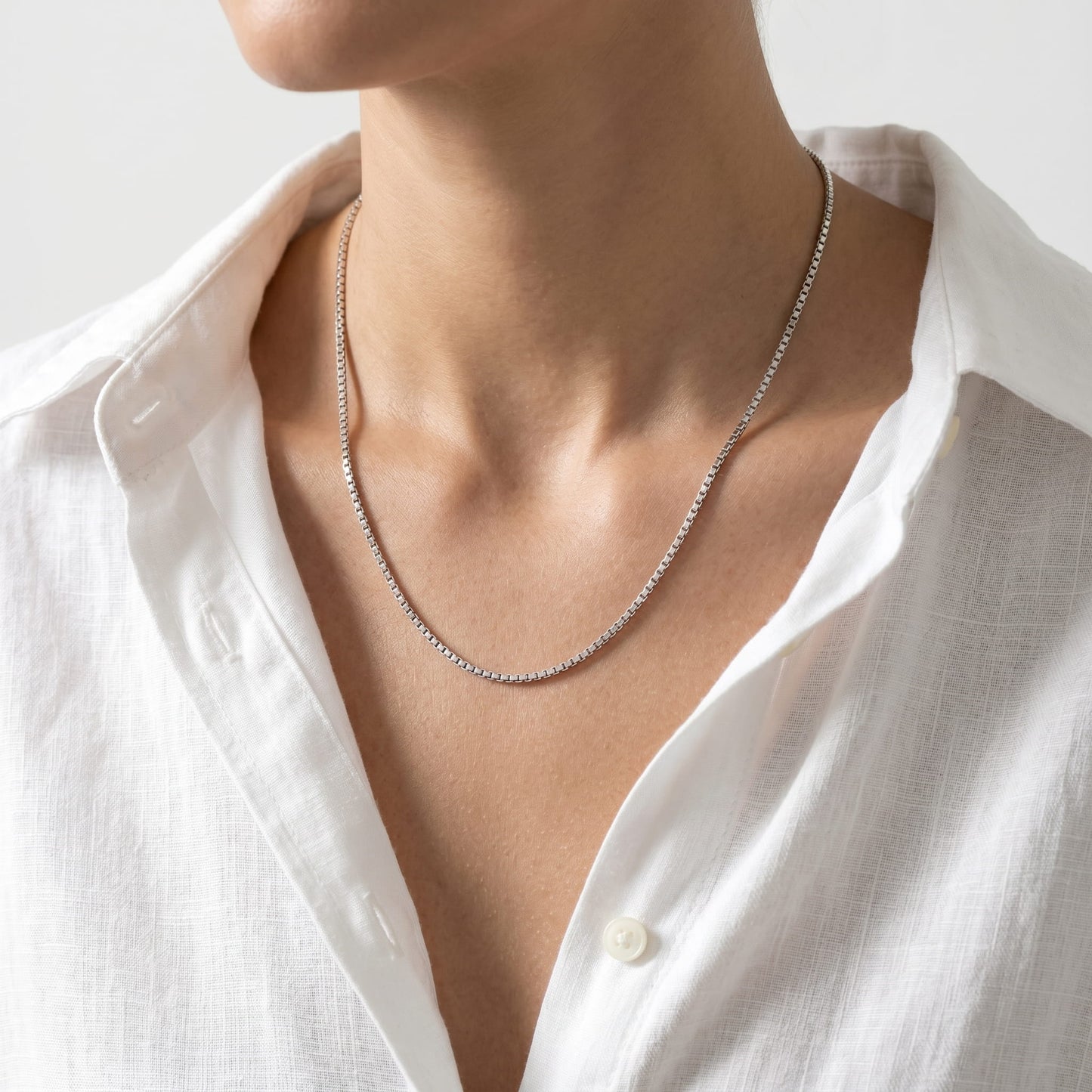 Person wearing a delicate silver necklace with a white shirt.