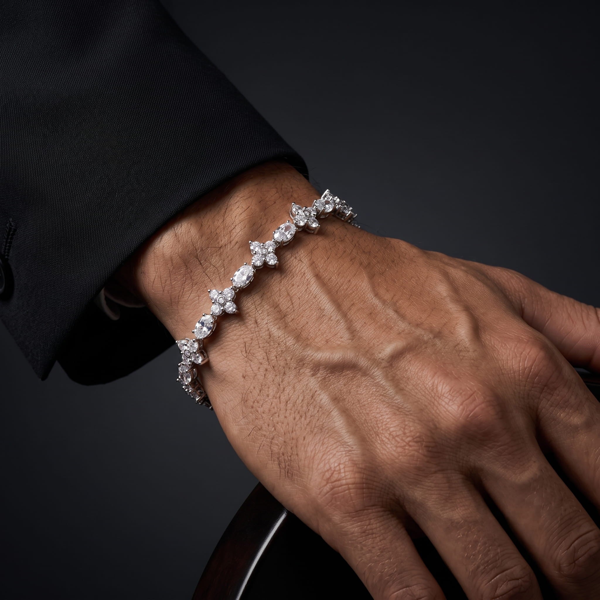 A close-up of a person's hand and wrist wearing a delicate silver-toned bracelet adorned with sparkling clear gemstones, set against a dark background.