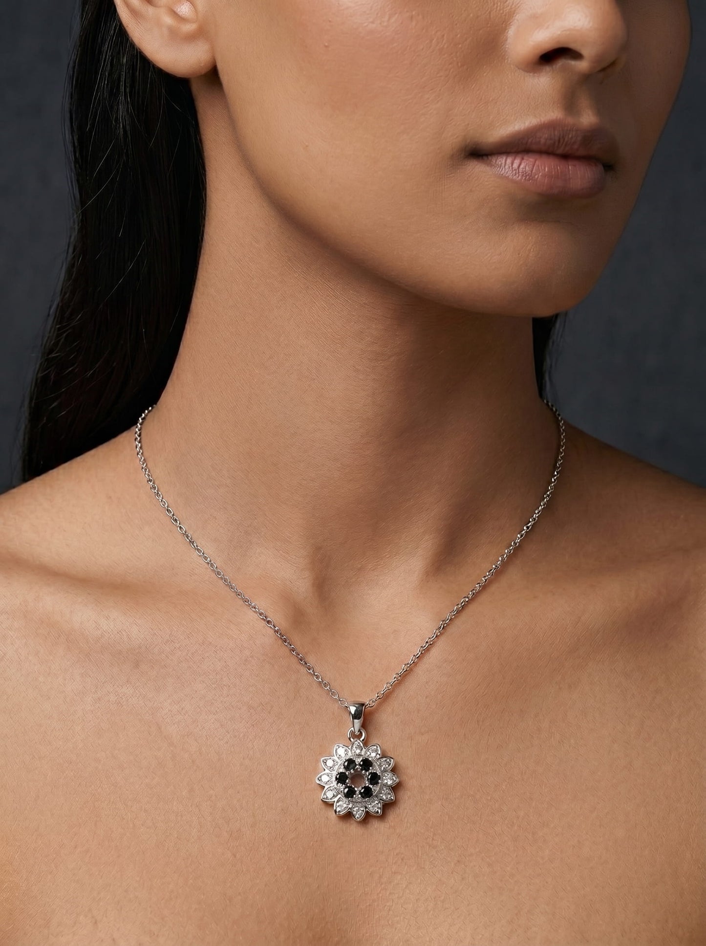 Close-up of a woman wearing a necklace with a floral pendant against a dark background